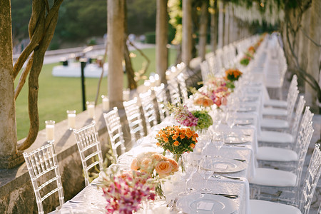 布达瓦里一张很长的婚宴桌 上面有黄色 橙色 粉红色玫瑰花束 玻璃椅子是用透明塑料制成的纸杯椅背景