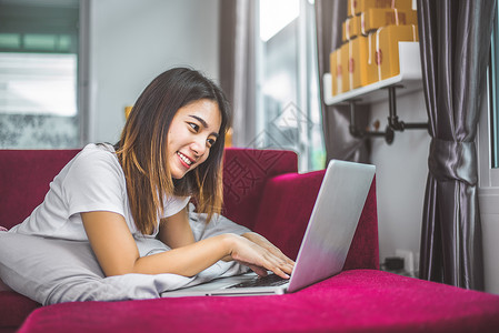 网上兼职素材年轻女子在红色沙发上用笔记本电脑上网 心情愉快 销售和网上购物的概念 商务人士和营销 新商业商务人士和企业家的幸福背景