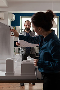 建筑工人用Maquette检查蓝图图建筑师经理职场女士会议职业办公室生意人讨论项目背景图片