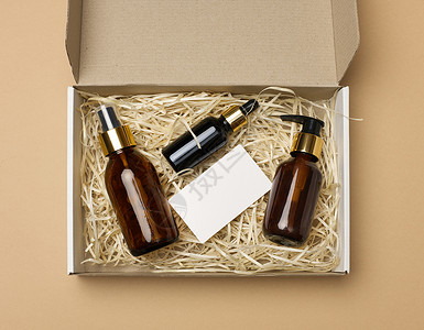 化妆品价格用于化妆品的棕色玻璃瓶和一张白纸空白名片位于米色背景的纸板纸盒中背景