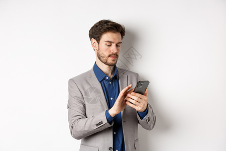 手机推销员穿着西装的年轻商务人士在手机上发短信 看着智能手机 站在白色背景下推销员工作电话男人生活广告男性工作室成功商务背景