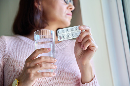 绝经在成年妇女手中紧闭装有水杯的水的泡泡药丸药物药店保健疼痛诊断治疗玻璃症状女性饮食背景