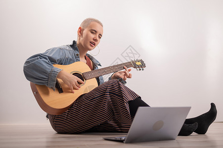 四弦吉他坐在家里地板上 在笔记本电脑上看吉他辅导课的年轻时装女青年 在隔离中远程学习音乐电影教程教育互联网歌曲女士视频网络技术女性背景