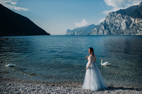 天鹅公主一名女性在意大利一座山和湖的背景下被拍到照片 TorboleTorbole 在Lake Garda湖的堤岸上行走天鹅山脉太阳衣服背景