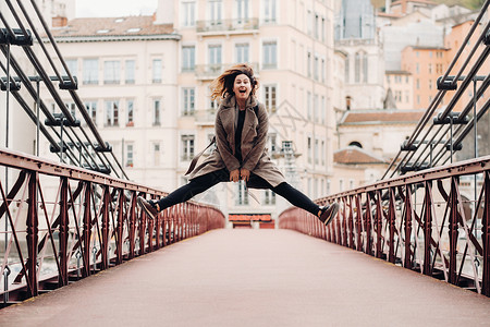跳桥素材在里昂老城的一座桥上 一个披着长发的大衣女孩激动地跳了起来 法国 一件外套的女孩在法国背景