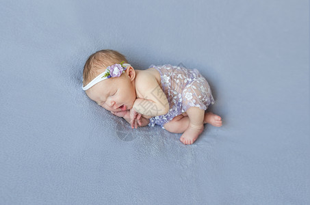 睡着有紫色面纱的可爱婴儿冒充女孩娘娘腔白色孩子舒适婴儿床花朵小憩新生背景图片