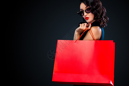 砸金蛋中红包黑周五商店的销售概念 戴墨镜的购物妇女拿着红包 在黑暗背景中被孤立黑色女孩购物狂消费者黑发购物中心快乐成人女性头发背景