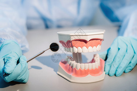 戴蓝色手套和面具的牙医拿着上下颌的牙科模型和牙镜卫生牙桥矫正牙科技师牙齿镜子技术员老年假牙塑料背景