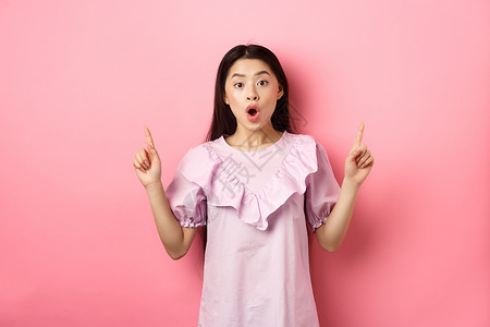 兴奋的亚洲青少年女孩举起手指 说哇和展示宣传协议 站在粉红背景上穿着着衣服购物促销广告学生工作室女性女士化妆品投标情感背景图片
