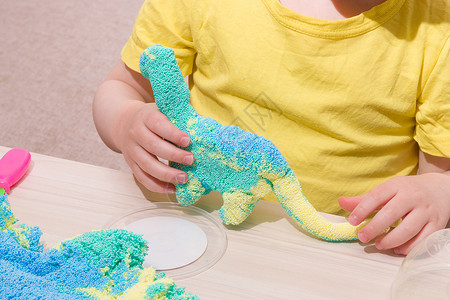 蓝色恐龙孩子在桌子上用聚合物颗粒玩橡皮泥 用小球做成的原始橡皮泥 孩子用橡皮泥玩恐龙 在家里和孩子玩什么手工业面团幼儿园游戏童年乐趣运动背景