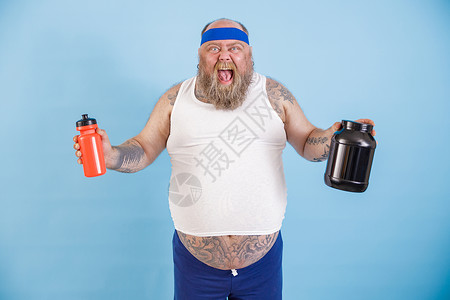 带头带的兴奋性大胖子 在演播室里拿着一瓶饮料和蛋白质补充品背景