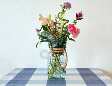 玻璃花瓶粉色花在靠近白墙的现代住宅中 玻璃花瓶中盛放着美丽 鲜艳 色彩缤纷的春花 桌上摆着粉红色和紫色的鲜艳花束 复古夏季装饰背景