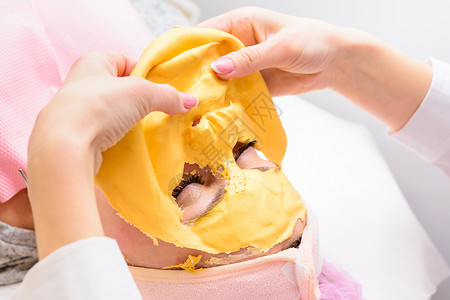 藻酸盐去除美容金质的工艺 在沙龙中消除化妆程序 笑声治疗女士护理手术果冻状面膜口罩病人整容金色背景