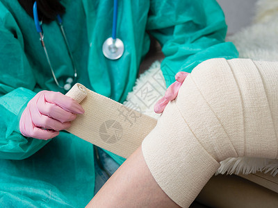创伤骨科一名戴着医用手套和口罩的护士在病人的腿和膝盖上缠绕着弹性绷带 外伤科医生在理疗室给病人使用弹性材料背景