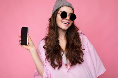 美丽微笑的年轻女性漂亮的照片穿着休闲时尚的服装站在孤立的背景与复制空间拿着智能手机显示手机在手与空屏幕显示用于模型看相机展示电话背景图片