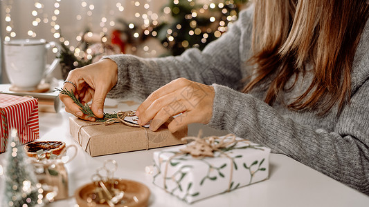 女人的手包裹着圣诞礼品盒 特写 白桌上未经准备的礼物 上面有装饰元素和圣诞或新年 DIY 包装概念背景图片