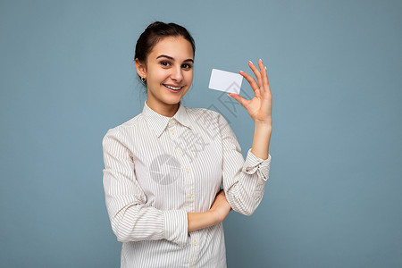 好评返现卡照片中 身穿蓝色背景中突显的白色衬衫 面带微笑的迷人黑发年轻女性拿着信用卡看着相机背景