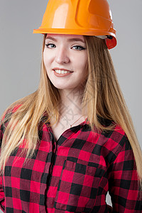 橙色格子一个年轻有魅力的女人的肖像 头戴橙色头盔金发 穿着中性灰色背景的金发成人女孩工作安全帽员工头发金发女郎职业工程女性背景