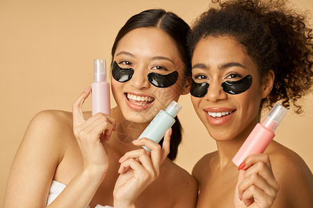 两个可爱的年轻女性 眼罩下含水凝胶的水凝胶 带着美容品装瓶子 在蜜蜂背景上与世隔绝背景图片