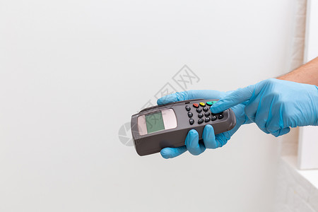 收银员手持信用卡阅读机 佩戴一次性手套 在Covid19大流行病期间用智能手机付费顾客手术现金客户近场支付电话安全商业卫生读者高清图片素材