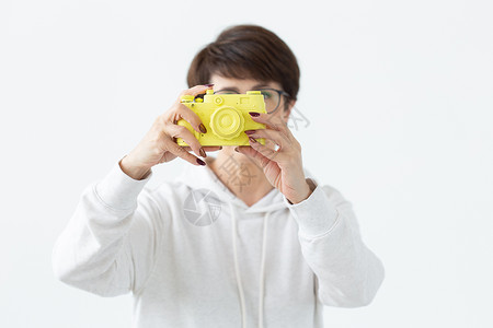 正能量照片戴眼镜的正能量中年妇女手里拿着一台摆在白色背景上的老式黄色相机 照片爱好者和爱好的概念成人眼镜胶片冒充微笑女性快乐发型喜悦黑发背景