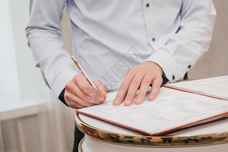 注册表证婚人男友在衬衫上的手把签名放在婚礼特写上成人男性协议朋友们桌子庆典写作合同文档新娘背景