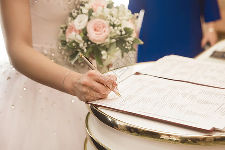 婚礼签名年轻女新娘的手在登记办公室的证件上签字表示同意结婚 并签署同意结婚书(签名)背景