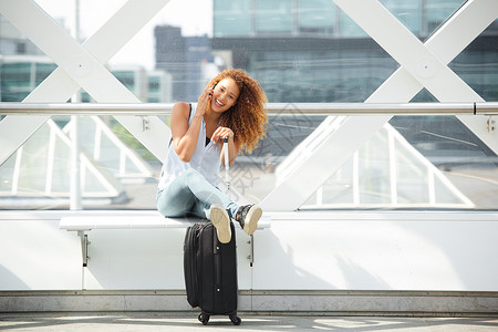 拿行李女孩快乐的旅行妇女坐着行李箱 在车站上接听手机背景