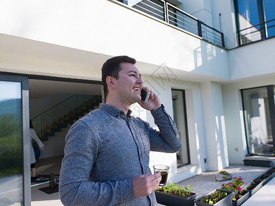 男人在豪华住宅别墅前使用手机屋主男性电话假期成人商务花园房子人士财产背景图片