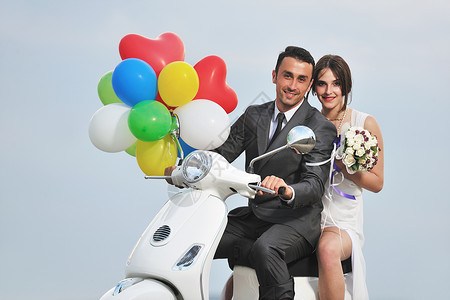 刚结婚的夫妇在海滩上骑白色摩托车车辆花朵婚姻成人微笑海岸气球农村黑发太阳镜背景图片