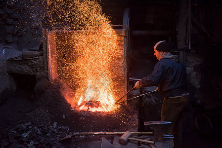热势难挡年轻的传统铁匠与开着的火一起工作男人煤炭金属建造工具工艺火花锤子橙子工人背景