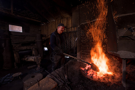 热势难挡年轻的传统铁匠与开着的火一起工作建造工具橙子工人市场火焰男人工匠制造业锤子背景