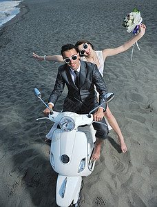 刚结婚的夫妇在海滩上骑白色摩托车新娘婚姻旅行男人喜悦微笑裙子车辆花朵夫妻背景图片