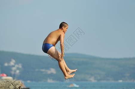 男孩跳海乐趣假期空气海岸自由孩子技巧男人喜悦蓝色背景