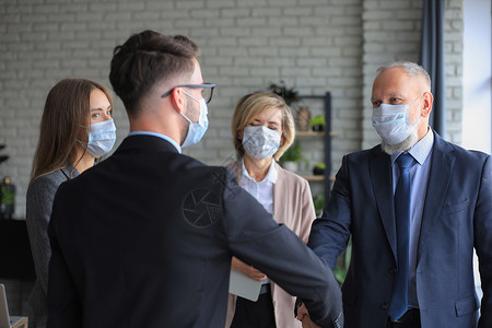 戴医疗面罩的商务人士握手 完成会议闭幕式金融顾客力量办公室合同笔记本微笑工作饮料团体背景图片
