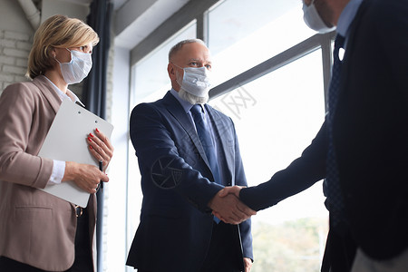 戴医疗面罩的商务人士握手 完成会议闭幕式团队团体夫妻笔记本银行玻璃律师力量金融男性背景图片