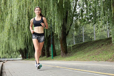 年轻运动女性在公园里慢跑训练赛跑者锻炼电话娱乐福利太阳身体运动员成人图片