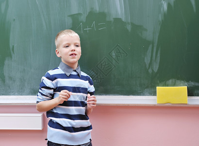 小学一年级数学班快乐的年轻男孩微笑思考测试男性黑色桌子牙齿知识黑板教育背景图片