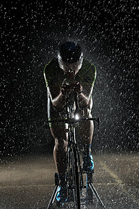 在雨夜快速骑着自行车的三亚马龙运动员活力赛车手黑色铁人天气钢铁侠男人头盔训练运动背景图片