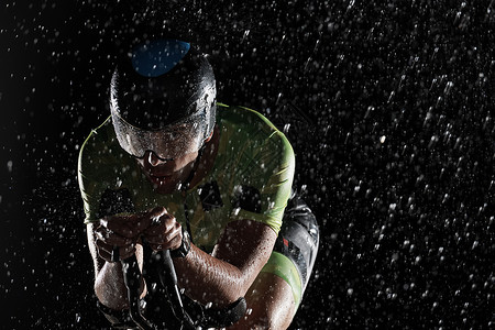 在雨夜快速骑着自行车的三亚马龙运动员天气速度训练运动头盔男人铁人钢铁侠耐力竞赛背景图片