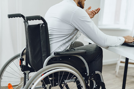 使用膝上型电脑坐在轮椅上的残疾男子工作人士成人车轮男性机动性互联网技术残障笔记本背景图片