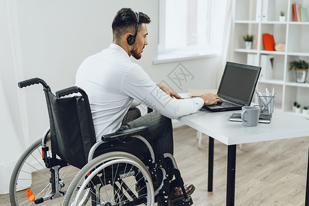 使用膝上型电脑坐在轮椅上的残疾男子残障互联网男性人士成人工作机动性工人技术车轮背景图片