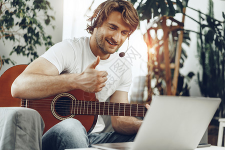 年轻人在电脑上看吉他辅导课分数公寓笔记本男人活动学习唱歌歌曲吉他手音乐家背景