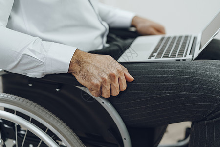 使用膝上型电脑坐在轮椅上的残疾男子机动性技术工人成人车轮人士男性残障工作互联网背景图片