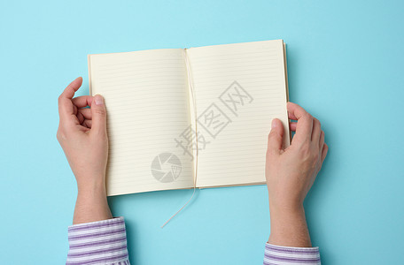 书张开的书两只女性手握着张开的笔记本 上面是蓝色背景 顶视图上的白白白空白页背景