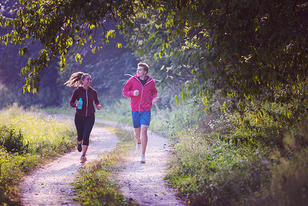 跑步森林在乡村公路上慢跑的年轻夫妇国家运动员活力赛跑者森林跑步自由阳光慢跑者冒险背景