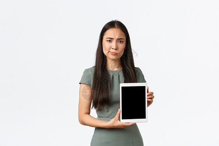 困惑和怀疑的亚洲女企业家对糟糕的统计数据感到失望 展示数字平板电脑屏幕 对申请评级不满意 傻笑和皱眉困扰 白色背景广告工作室示范背景图片