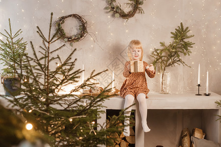 斯堪的纳维亚语包屑的一个女孩在圣诞节前夕在一个为新年节日装饰的美丽房子里玩耍 斯堪的纳维亚式的内地有活林树和木质楼梯脚步硬木圣诞礼物金发女郎彩灯衣冠背景