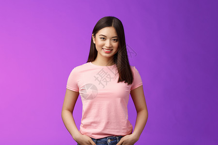 紫色口袋边框可爱柔弱的亚洲女性深色短发 站着粉红色 T 恤 手拿牛仔裤口袋 开心地微笑 保持有趣的谈话 站着紫色背景乐观大学青年黑发旅行商业背景