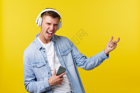 耳机促销x展架休闲 技术和应用广告概念 兴奋快乐的金发男人享受美妙的音乐 戴着耳机听歌 拿着手机 用隐形吉他弹奏背景